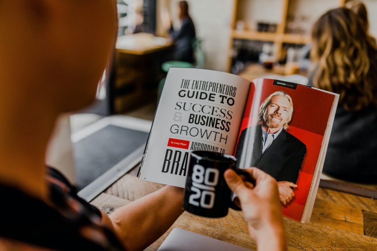 Man reading business strategy article in magazine and holding coffeecup imprinted with 80 20